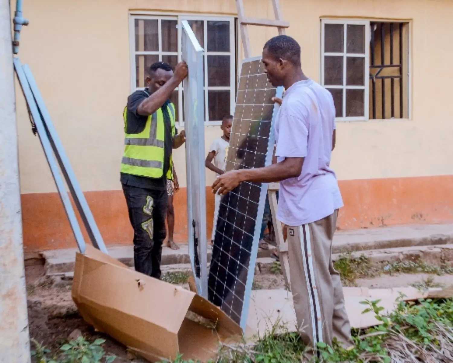 Solfa Power technicians carrying a large solar panel outside a building