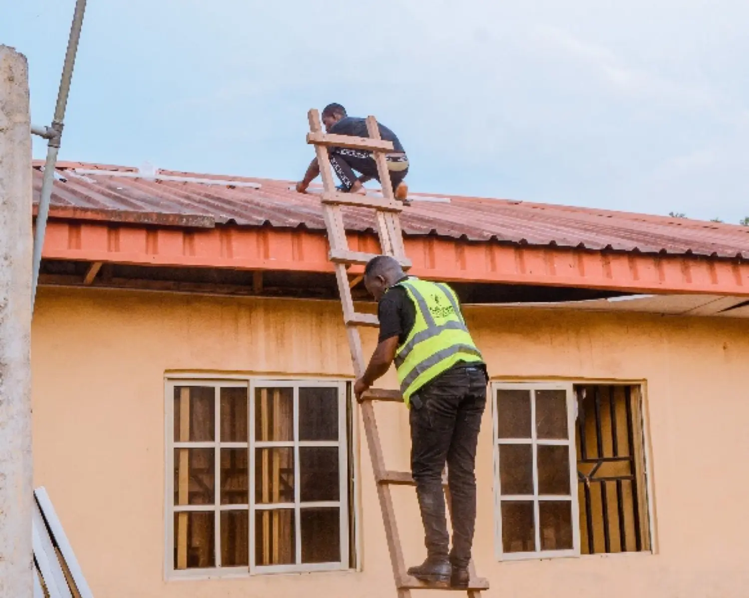 Two Solfa Power technicians installing solar panels on a rooftop, one climbing a ladder in a hi-vis vest